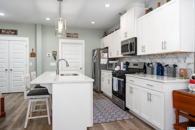 kitchen with white cabinetry, sink, decorative light fixtures, a kitchen island with sink, and appliances with stainless steel finishes