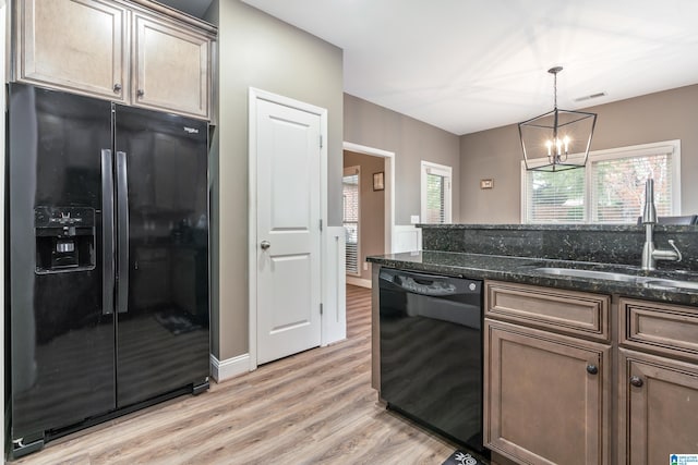 kitchen featuring an inviting chandelier, black appliances, sink, dark stone countertops, and light hardwood / wood-style floors