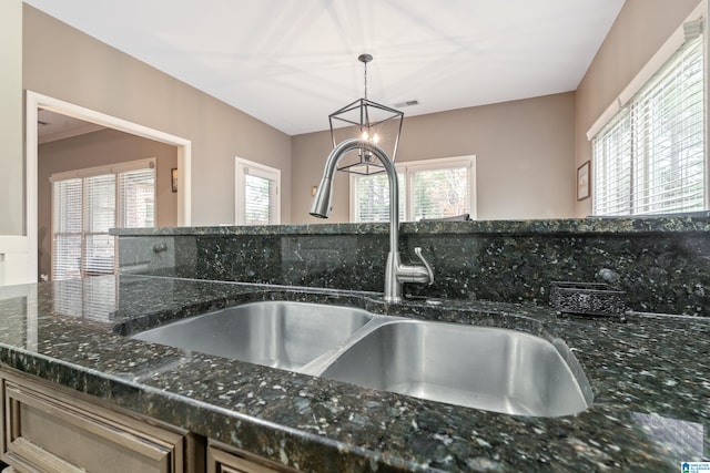 room details with sink, a notable chandelier, dark stone countertops, and hanging light fixtures