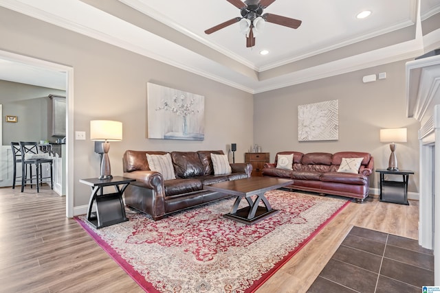 living room featuring hardwood / wood-style flooring, ceiling fan, crown molding, and a tray ceiling