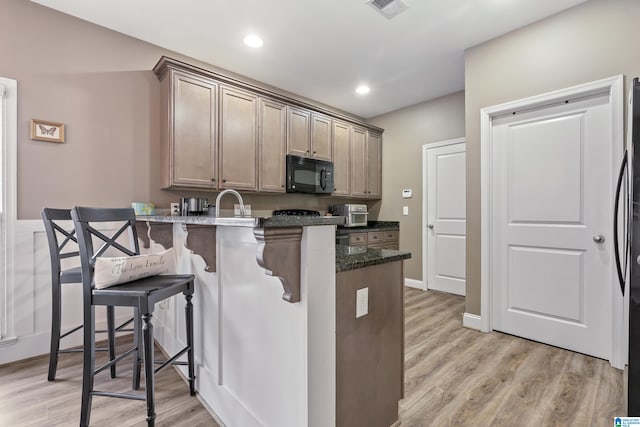 kitchen with sink, light hardwood / wood-style flooring, dark stone countertops, kitchen peninsula, and a kitchen bar