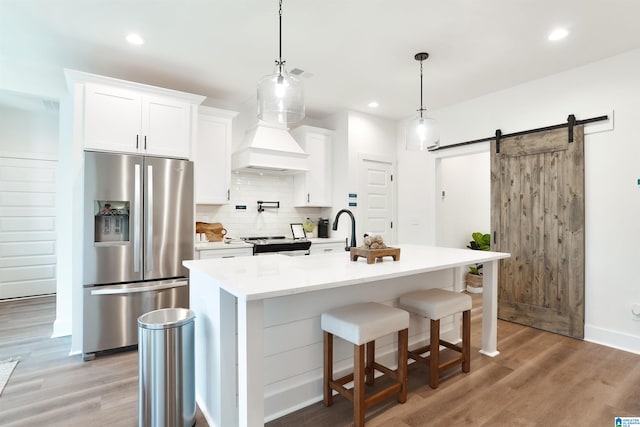 kitchen with a center island with sink, a barn door, white cabinets, and appliances with stainless steel finishes