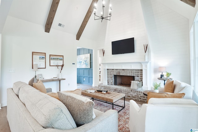 living room with a brick fireplace, beamed ceiling, high vaulted ceiling, a notable chandelier, and light hardwood / wood-style floors