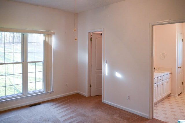 unfurnished bedroom featuring light carpet, connected bathroom, and sink