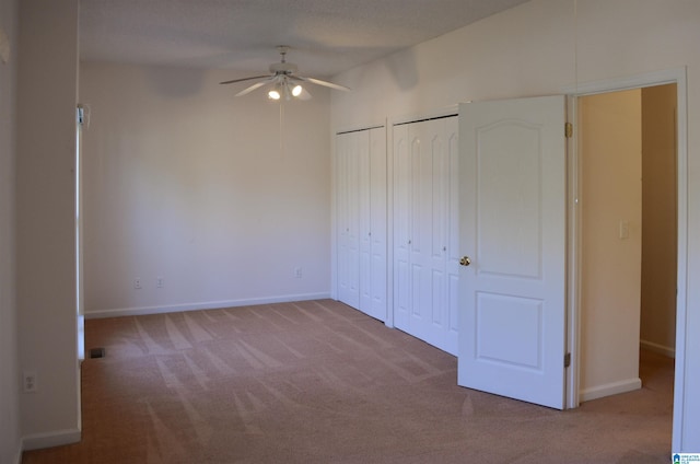 unfurnished bedroom with ceiling fan, light colored carpet, and two closets