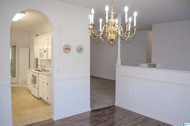 kitchen featuring white appliances, light tile patterned floors, hanging light fixtures, and white cabinets