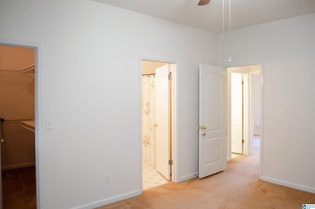 unfurnished bedroom with connected bathroom, a walk in closet, light carpet, a closet, and ceiling fan