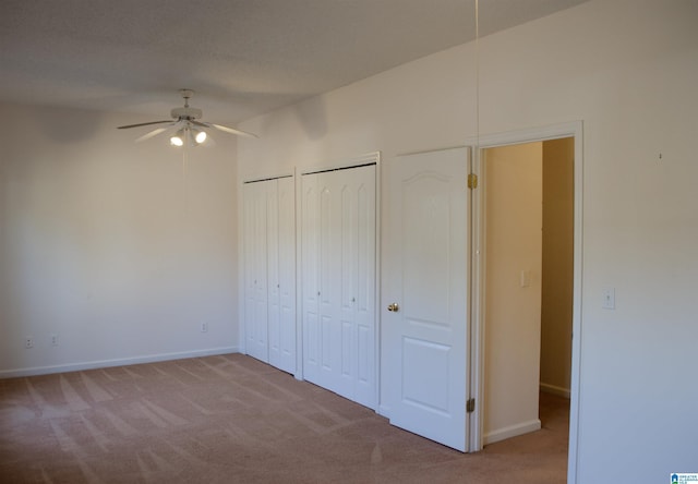 unfurnished bedroom featuring ceiling fan, light colored carpet, and two closets