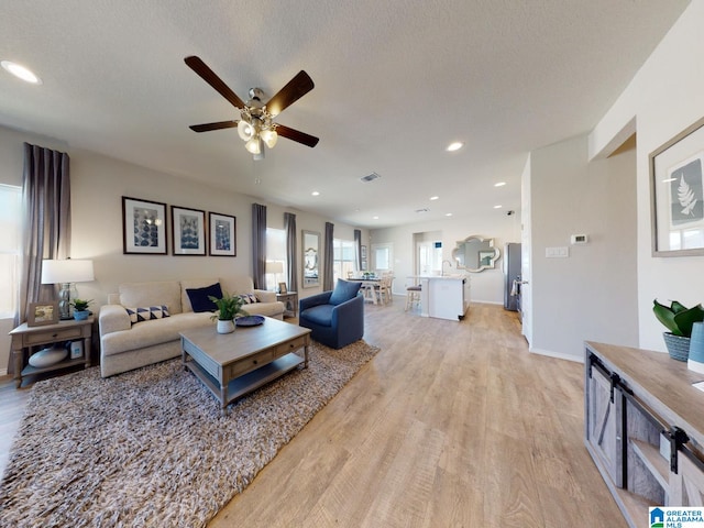 living room with ceiling fan, light hardwood / wood-style flooring, and a textured ceiling