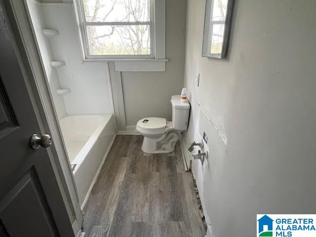 bathroom with a tub to relax in, hardwood / wood-style flooring, and toilet