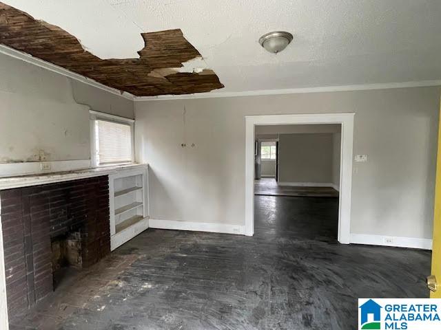 unfurnished living room with a textured ceiling, a brick fireplace, and crown molding