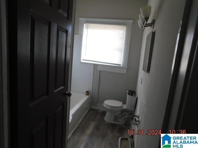 bathroom with a washtub, toilet, and wood-type flooring