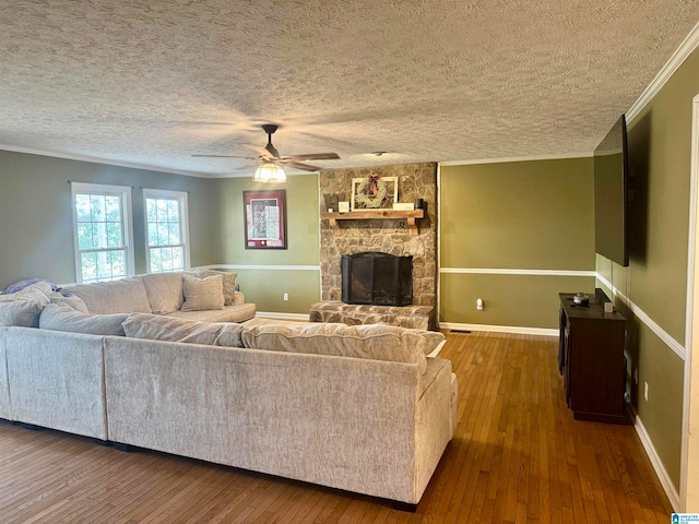 living room featuring a textured ceiling, ceiling fan, crown molding, dark wood-type flooring, and a stone fireplace