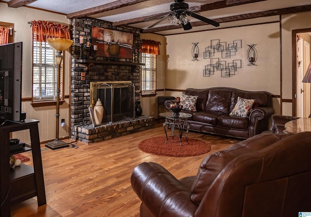 living room featuring a fireplace, a textured ceiling, ceiling fan, wood-type flooring, and beamed ceiling