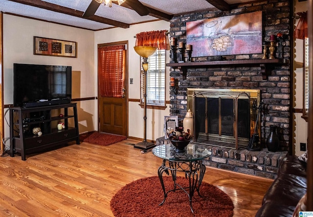 living room with hardwood / wood-style flooring, ceiling fan, a fireplace, a textured ceiling, and beam ceiling