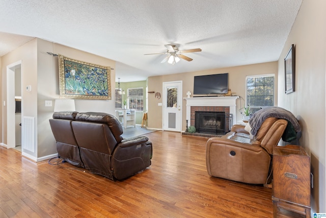 living room featuring ceiling fan, wood-type flooring, a textured ceiling, and a brick fireplace