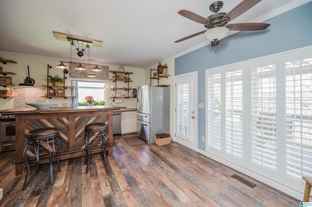 kitchen with a breakfast bar, crown molding, hardwood / wood-style flooring, appliances with stainless steel finishes, and white cabinetry