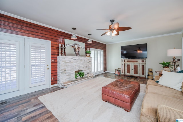 living room featuring wooden walls, hardwood / wood-style flooring, ceiling fan, ornamental molding, and a fireplace