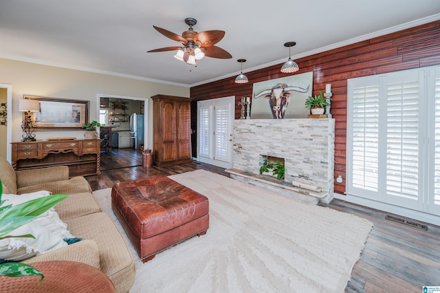 living room with ceiling fan, a stone fireplace, hardwood / wood-style floors, wooden walls, and ornamental molding