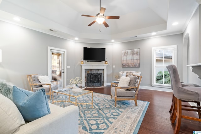 living room featuring a tile fireplace, a tray ceiling, plenty of natural light, and dark wood-type flooring