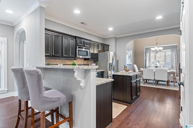 kitchen with dark hardwood / wood-style flooring, a breakfast bar, stainless steel appliances, an inviting chandelier, and a center island