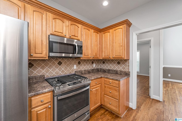 kitchen with wood-type flooring, stainless steel appliances, dark stone counters, and tasteful backsplash