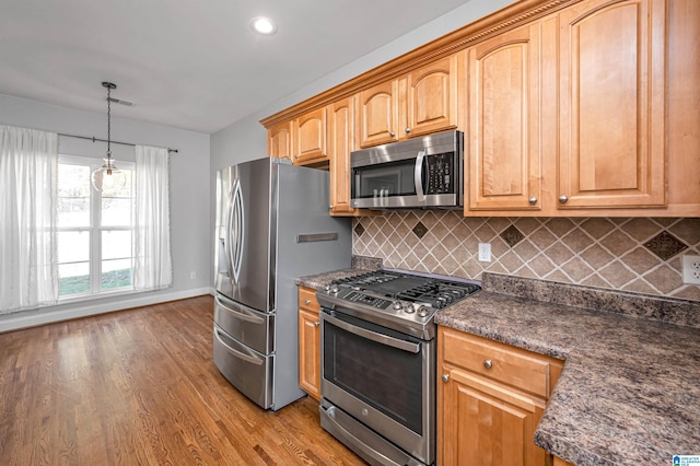 kitchen featuring appliances with stainless steel finishes, decorative light fixtures, tasteful backsplash, and light hardwood / wood-style floors