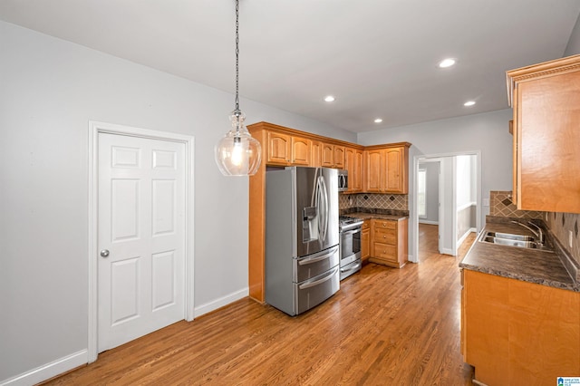 kitchen featuring sink, stainless steel appliances, tasteful backsplash, light hardwood / wood-style flooring, and pendant lighting