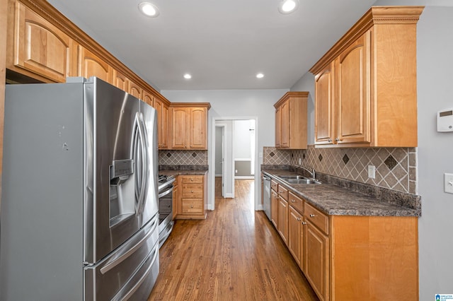 kitchen with backsplash, stainless steel appliances, sink, wood-type flooring, and dark stone countertops