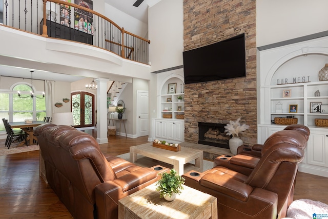 living room featuring dark hardwood / wood-style flooring, built in shelves, a notable chandelier, a high ceiling, and a stone fireplace