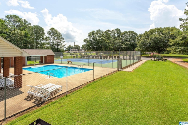 view of swimming pool with tennis court and a lawn