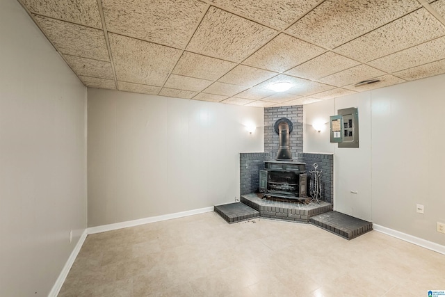 unfurnished living room with a wood stove, a paneled ceiling, and electric panel