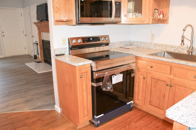 kitchen with sink, light hardwood / wood-style flooring, light stone countertops, and appliances with stainless steel finishes