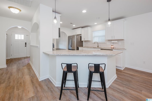 kitchen with white cabinets, stainless steel fridge, light hardwood / wood-style floors, and pendant lighting