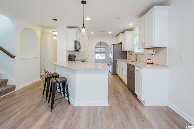 kitchen featuring hanging light fixtures, light hardwood / wood-style flooring, white cabinets, and stainless steel appliances