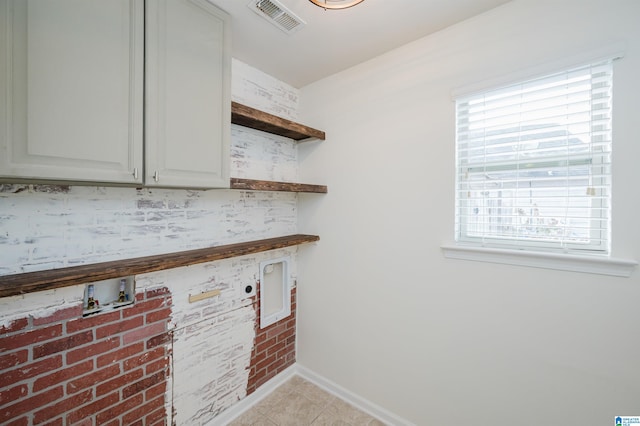 laundry area with a wealth of natural light, hookup for a washing machine, light tile patterned floors, and cabinets