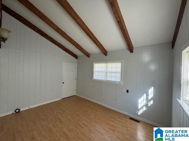 unfurnished room with lofted ceiling with beams, wood walls, and light hardwood / wood-style floors