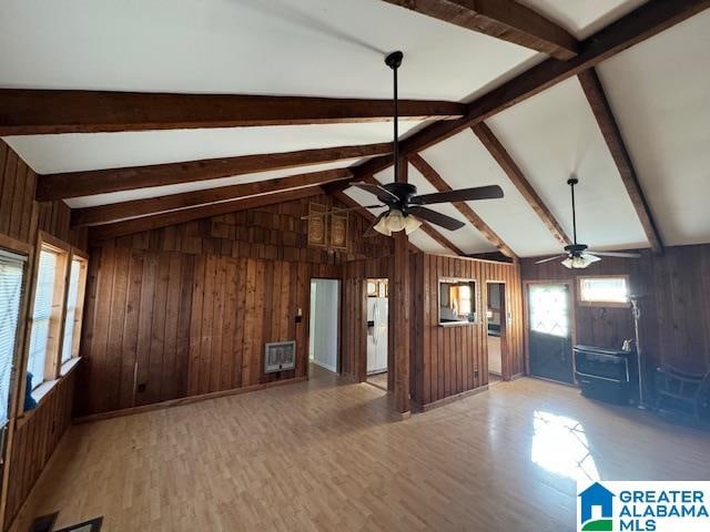 unfurnished living room featuring wood walls, hardwood / wood-style floors, ceiling fan, and lofted ceiling with beams