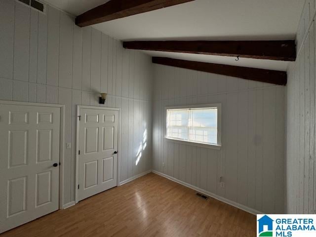 unfurnished room with hardwood / wood-style floors, vaulted ceiling with beams, and wood walls