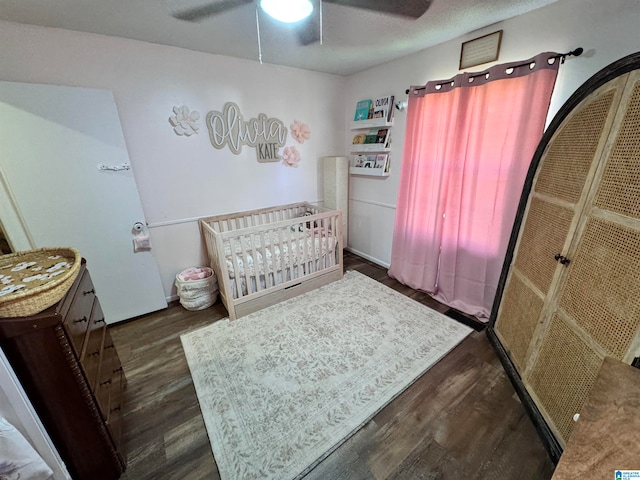 bedroom with a textured ceiling, ceiling fan, a nursery area, and dark hardwood / wood-style floors