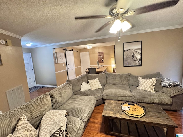 living room featuring a textured ceiling, ceiling fan, crown molding, a barn door, and dark hardwood / wood-style floors