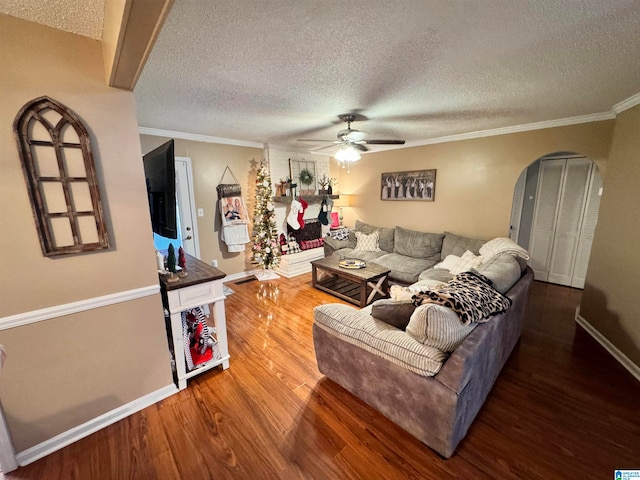 living room with a textured ceiling, crown molding, ceiling fan, and dark wood-type flooring