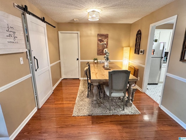 dining area with a barn door, wood-type flooring, a textured ceiling, and a notable chandelier