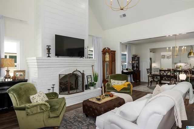 living room with a brick fireplace, an inviting chandelier, dark hardwood / wood-style floors, and high vaulted ceiling