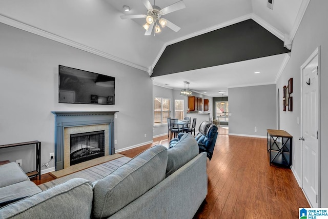 living room with ceiling fan, wood-type flooring, vaulted ceiling, a tiled fireplace, and ornamental molding