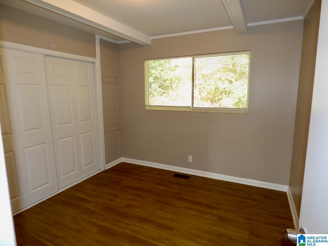 unfurnished bedroom featuring a closet, dark hardwood / wood-style flooring, beamed ceiling, and crown molding