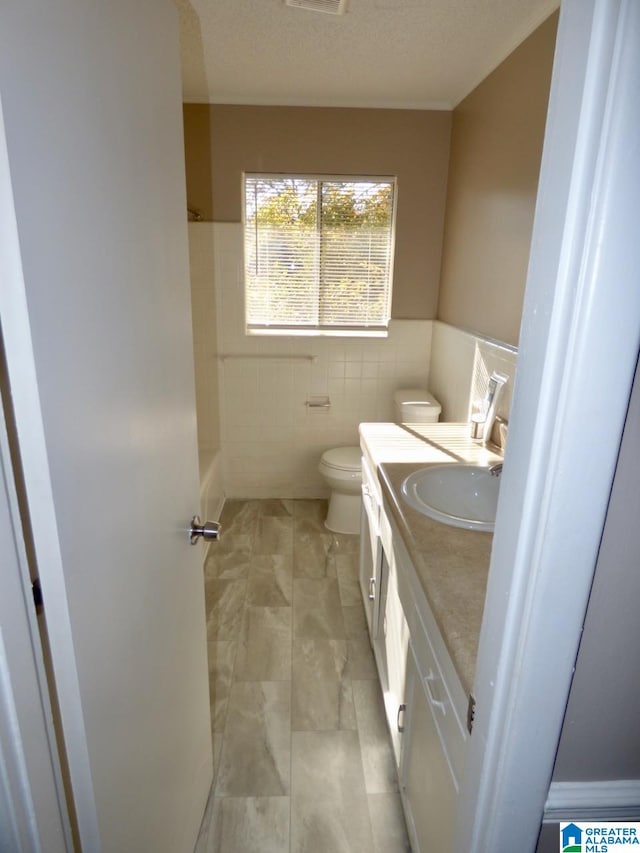 bathroom featuring a textured ceiling, vanity, tile walls, and toilet