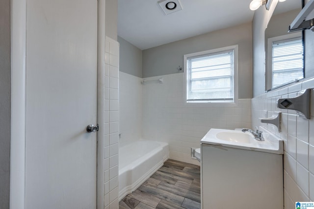 full bathroom featuring vanity, tiled shower / bath combo, hardwood / wood-style flooring, tile walls, and toilet