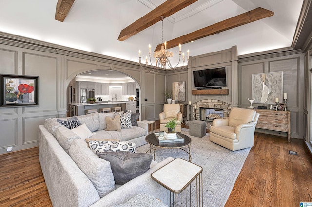 living room featuring beam ceiling, an inviting chandelier, dark hardwood / wood-style flooring, a fireplace, and ornamental molding