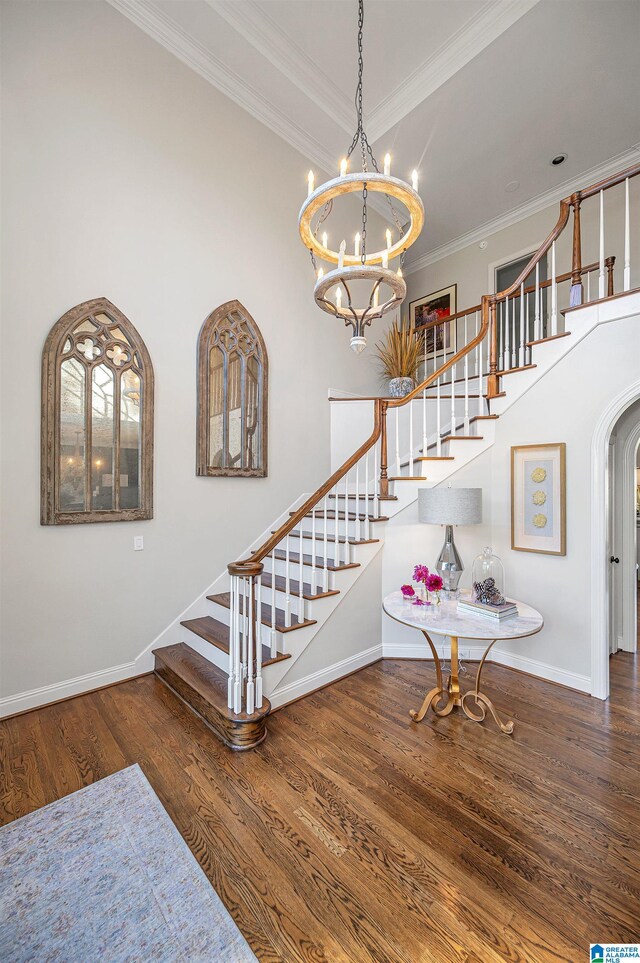 stairway with hardwood / wood-style flooring, ornamental molding, a towering ceiling, and an inviting chandelier